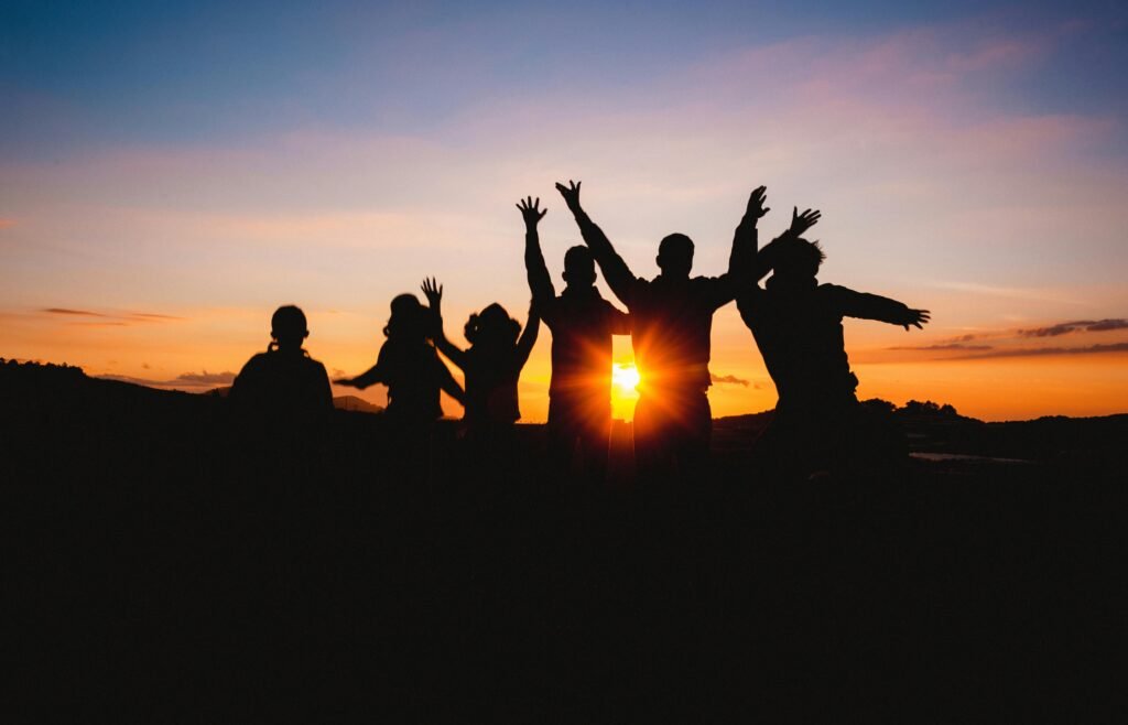 Group of friends silhouetted against a vibrant sunset sky, celebrating together outdoors.